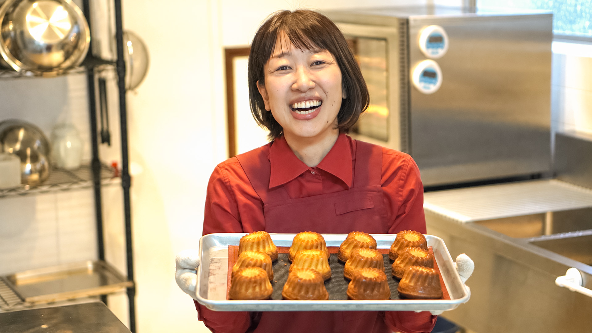 焼きたてのマフィンの天板を持って笑うスタッフ